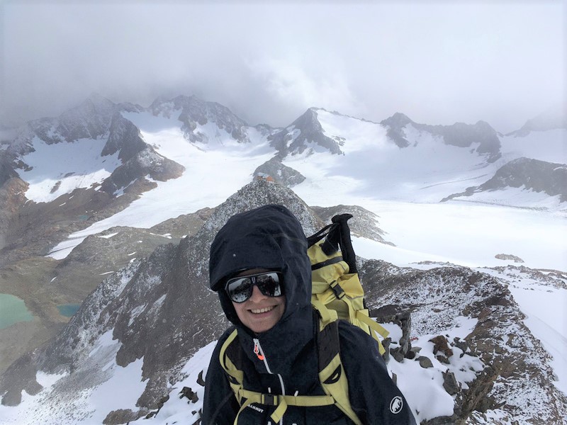 Antonia Messerschmitt steht im Bergsteigerdress über schneebedeckten Alpengipfeln