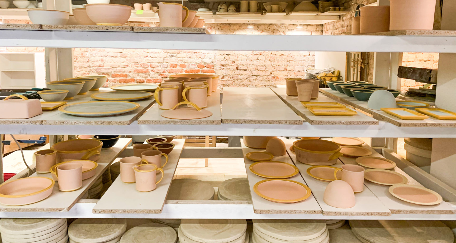 Zahlreiche bemalte Tassen, Teller und andere Keramik in einem Regal zum trocknen.