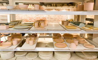 Zahlreiche bemalte Tassen, Teller und andere Keramik in einem Regal zum trocknen.