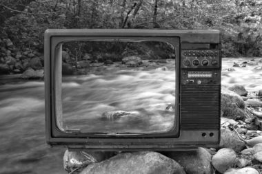 Fernseher ohne Glas vor verschwommenem Gewässer mit starker Strömung in schwarz weiß